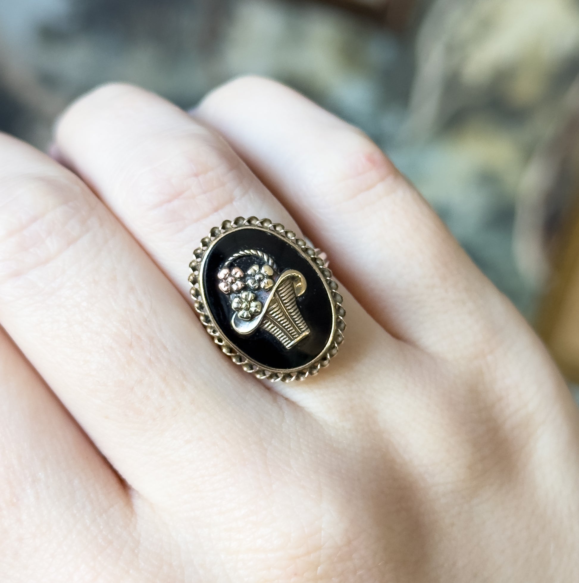 Shown on a finger against a blurred backdrop, the oval face covering most of the finger's width, giving a sense of its scale with the basket and flowers facing the camera.