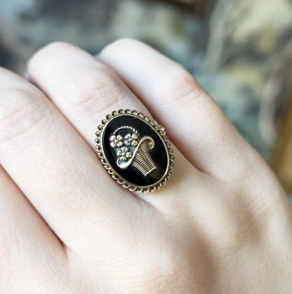 Shown on a finger against a blurred backdrop, the oval face covering most of the finger's width, giving a sense of its scale with the basket and flowers facing the camera.