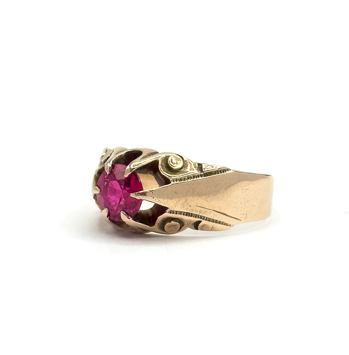 Low side view with the round pinkish red stone at the left, each prong of the raised head clearly gripping its edge as the engraved shoulder widens into the polished band at the right.