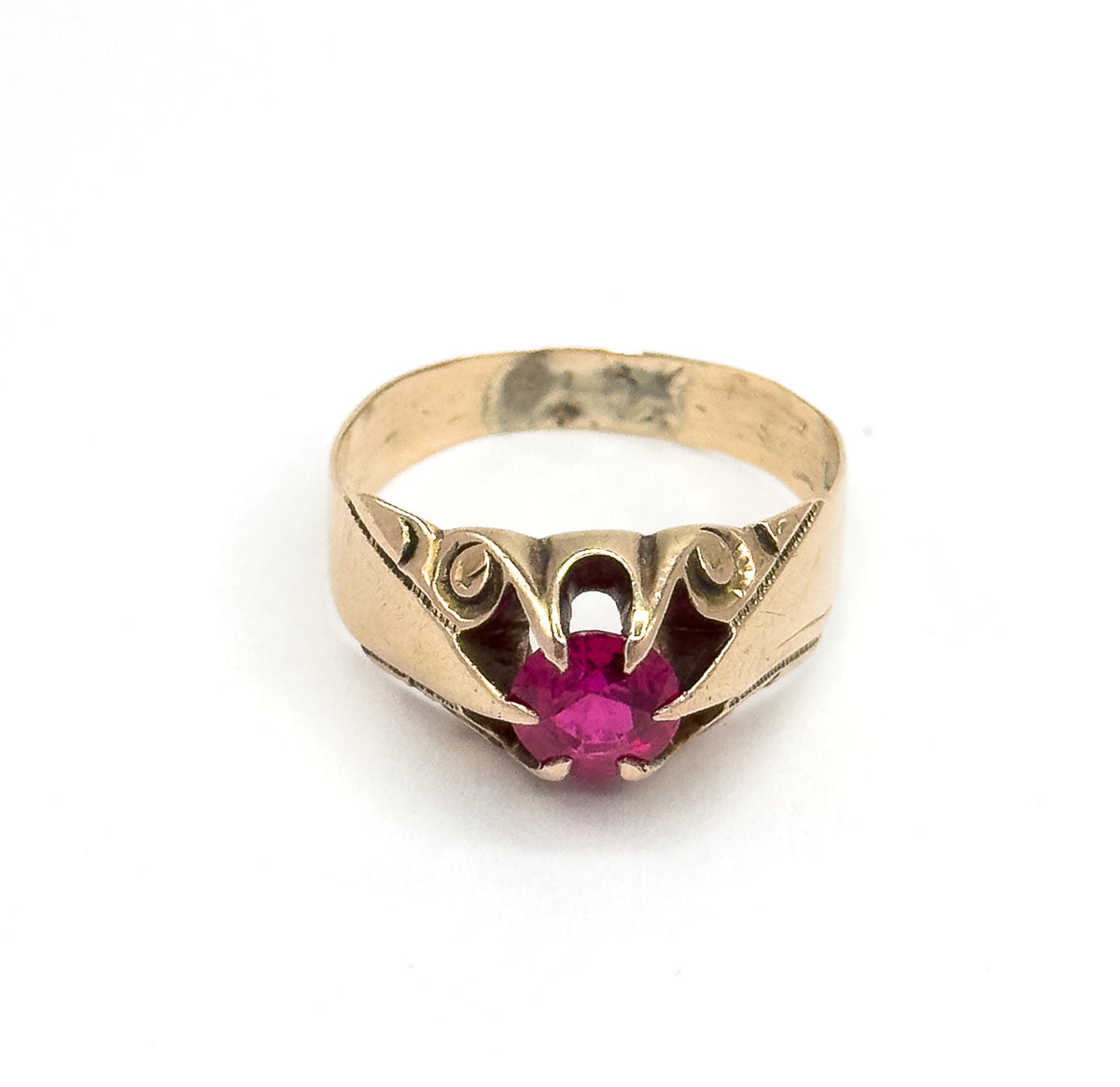Head-on from the front, the round pinkish red stone sits low in its four-prong head with the engraved swirls curving symmetrically to either side and the yellow band arching above.