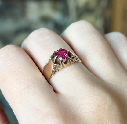 Angled from above with the hand filling the frame for scale, the wide band spans the finger and the pinkish red stone catches light between its four prongs.