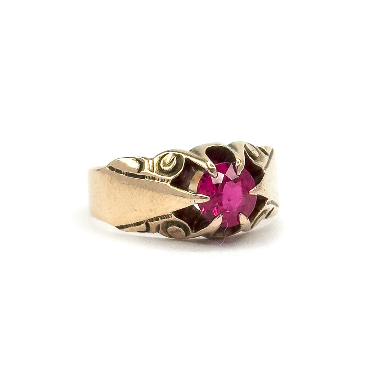 Off the hand against white, the ring stands side-on so the wide polished shank rises into the swirl-engraved shoulders and the four-prong head holding the pinkish red stone.