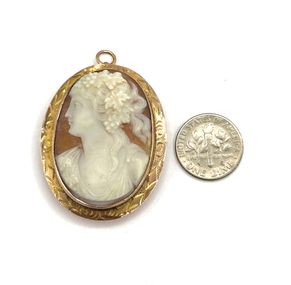 Front view laid flat beside a dime, the oval cameo and its engraved gold frame standing about twice the coin's width, with the small round bail at the top.