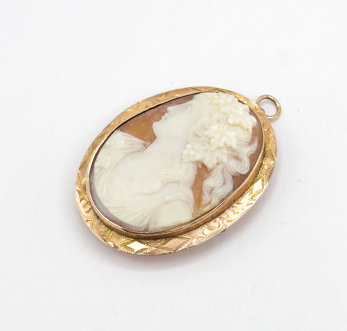 Angled three-quarter view on white, the oval tilted so the hand-engraved scrollwork along the side of the gold frame and the round bail at the upper right both catch the light.