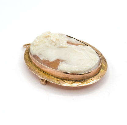 Tipped-back three-quarter view from above, the full oval visible at an angle so the stepped inner bezel and engraved outer rim ring the carving, with the bail at upper left and catch at lower left.
