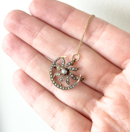 Front view resting on open fingers for scale, the seed pearl crescent curving around the sunburst rays with the old European cut diamond at its centre and the chain running over the palm.