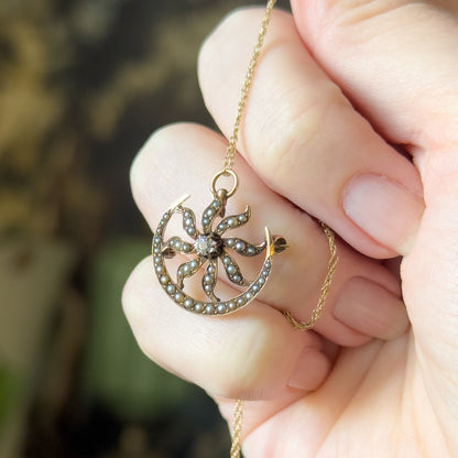 Close view held between fingertips, the pendant tilted so the pin catch and bail sit against the skin and the graduated cream and grey seed pearls fill the frame.