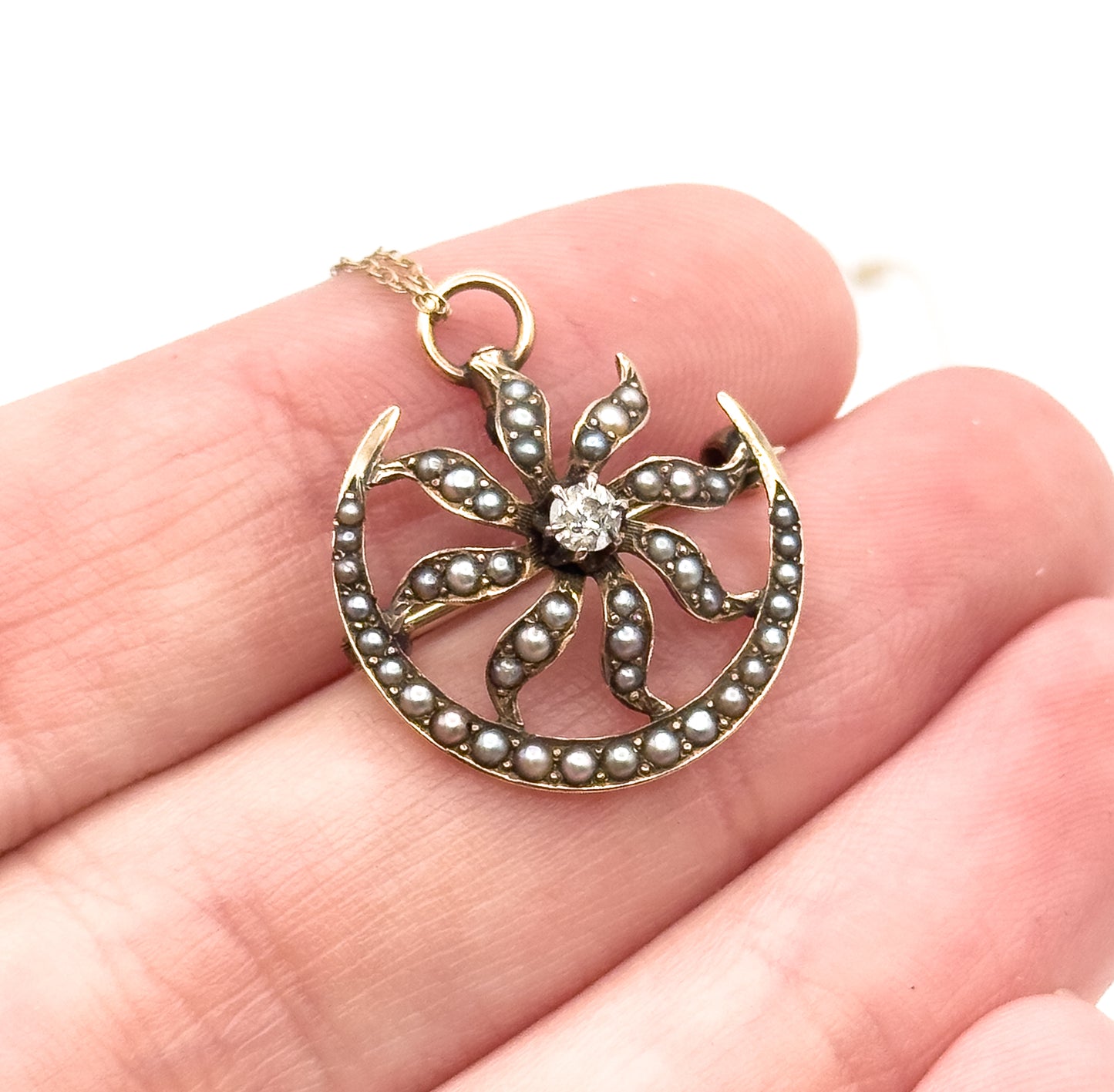 Resting flat across the fingertips at a slight tilt, the pendant spanning barely more than a fingertip's width, with the chain rising from the ring bail towards the upper corner.
