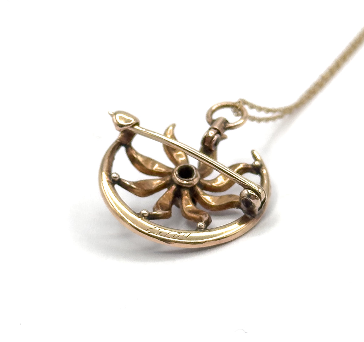 Edwardian sunburst and crescent pendant in 10 karat gold, shown from the back on a white ground with its hinged pin stem, catch, bail and chain visible.