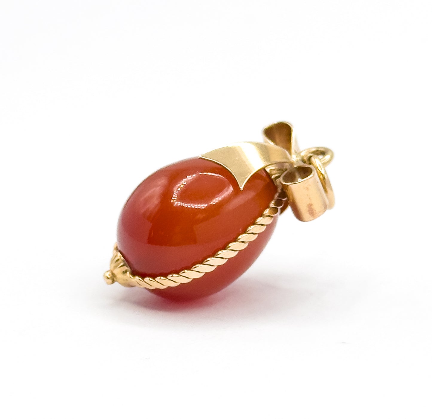 Side-on view with the charm lying almost horizontal on white, showing the tubular bail and jump ring at the right and the cable wire curving under the carnelian egg's belly.