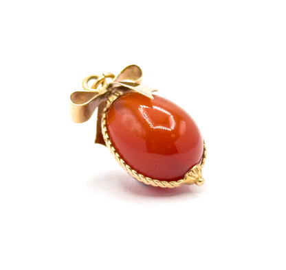 Tilted three-quarter view on white, the twisted cable wire tracing the egg's lower edge to a small gold bead at the base, with the bow and jump ring set back at the top left.