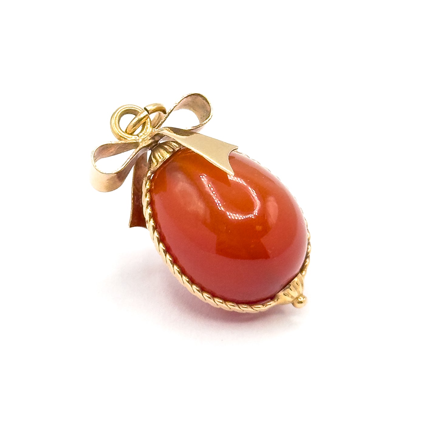 Tilted three-quarter view on white, showing the domed profile of the carnelian egg, the cable wire running along its side and the small beaded tip at the base of the gold mount.
