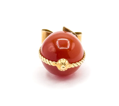 Close crop head-on with the carnelian egg filling the frame, the twisted cable wire crossing its lower half to a fluted gold cap and bead at centre, the bow's gold loops rising behind the top.
