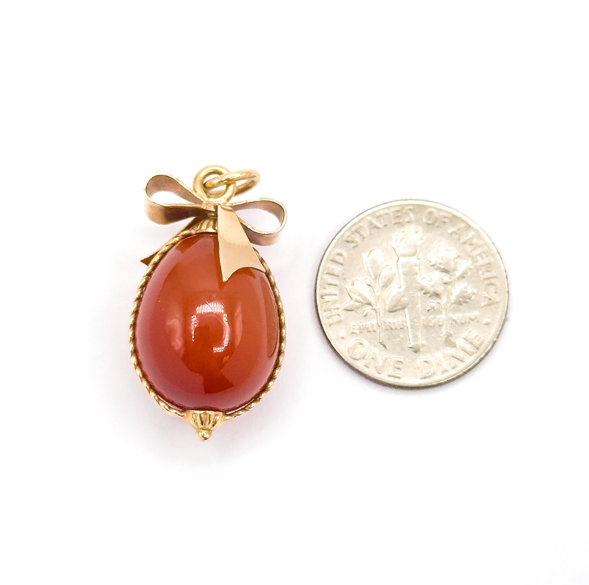 Shown next to a dime on white for scale, the carnelian egg alone about the size of the coin and the gold bow and jump ring adding roughly half again to the charm's height.