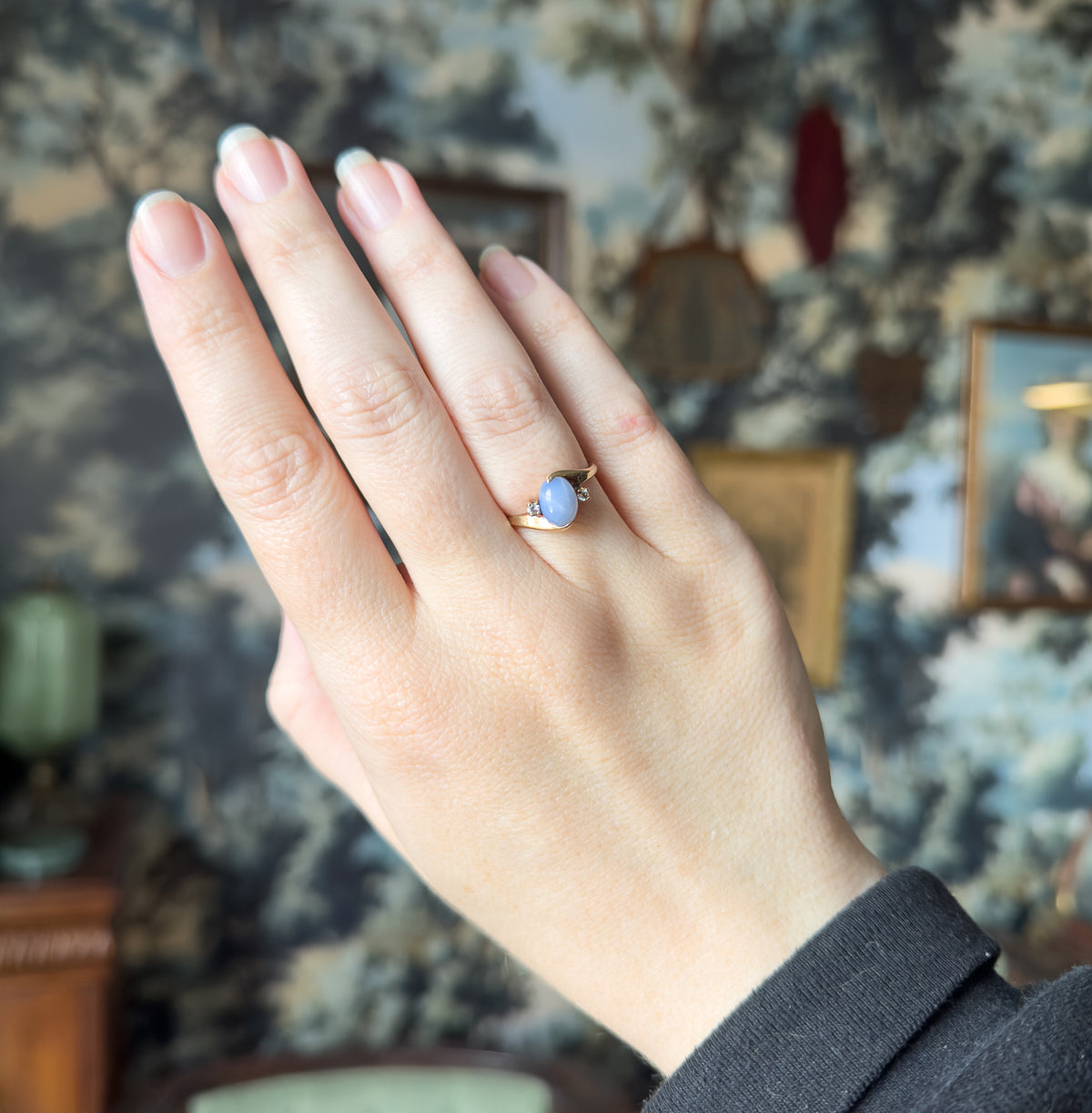 Full hand raised against a patterned backdrop, the ring small on the ring finger, giving a clear sense of its scale against the other fingers.