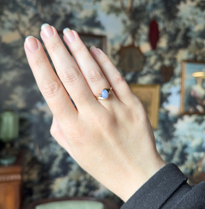 Full hand raised against a patterned backdrop, the ring small on the ring finger, giving a clear sense of its scale against the other fingers.