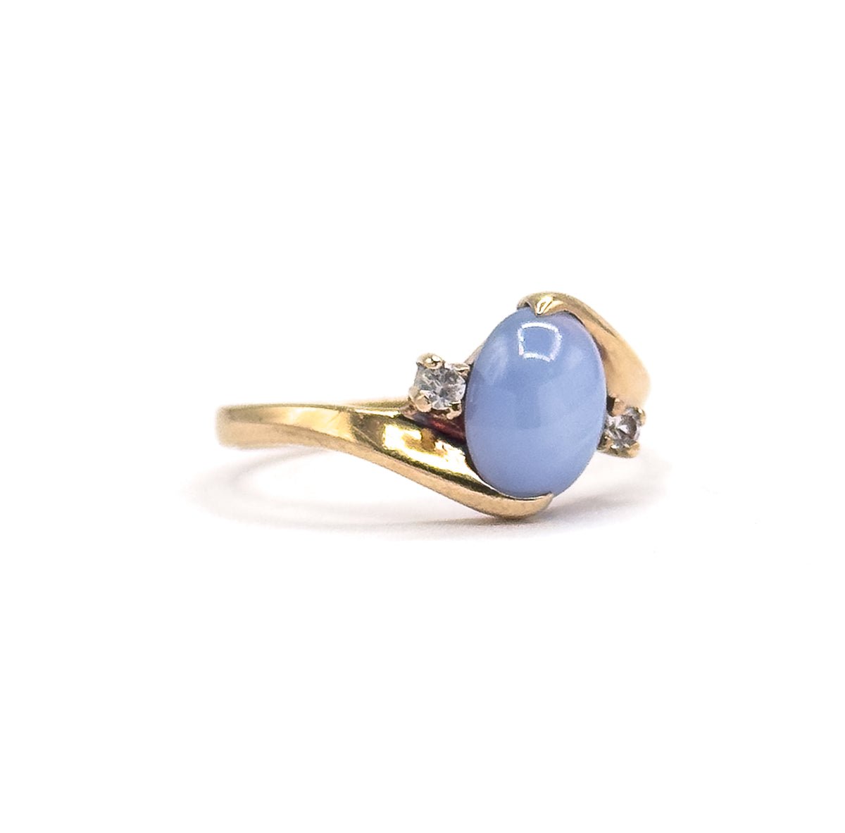 Side profile against a plain white background, the domed periwinkle cabochon sitting high in its prongs above the curving gold shank, one spinel visible on each side.