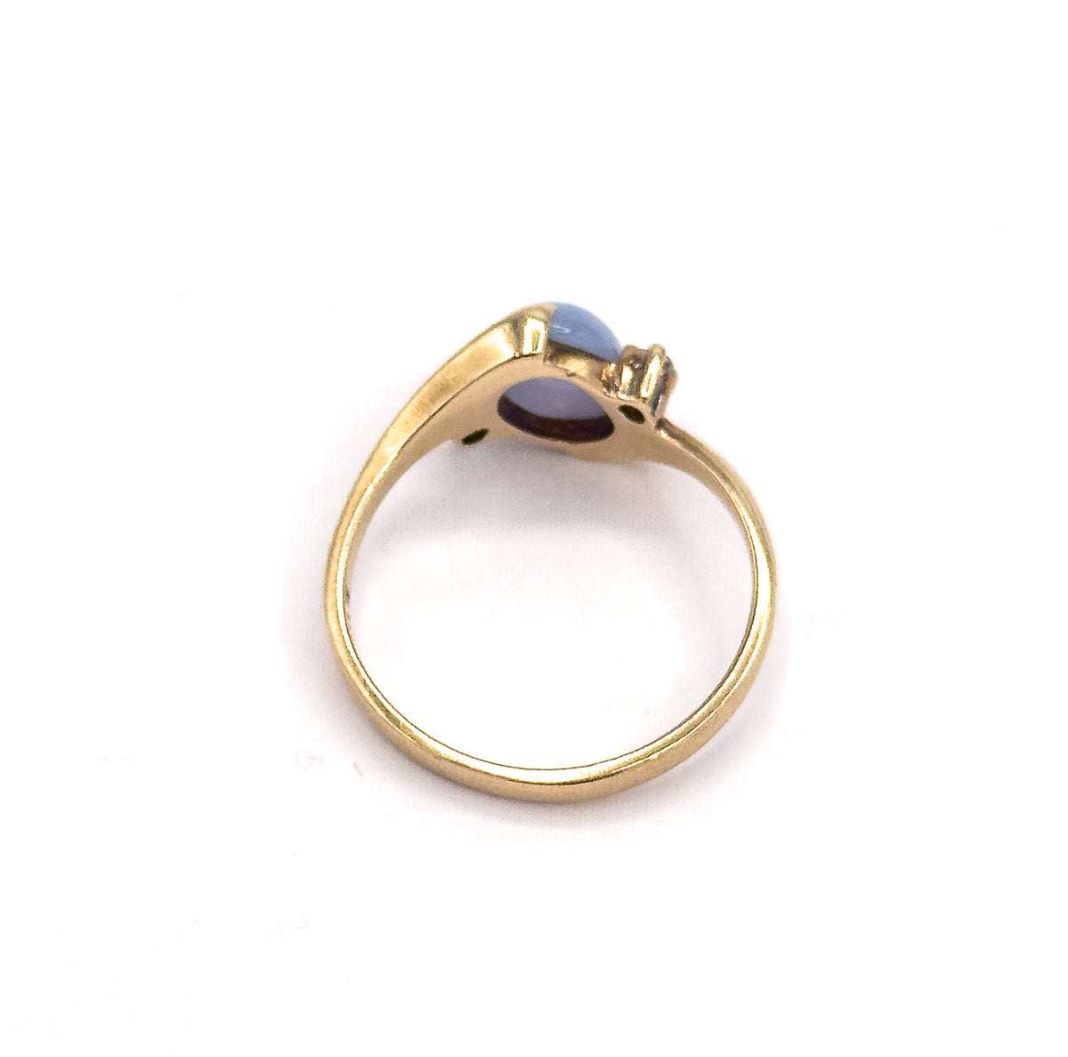 Rear view against white, looking through the open circle of the shank to the underside of the setting, where the back of the periwinkle cabochon and one small colourless spinel show.