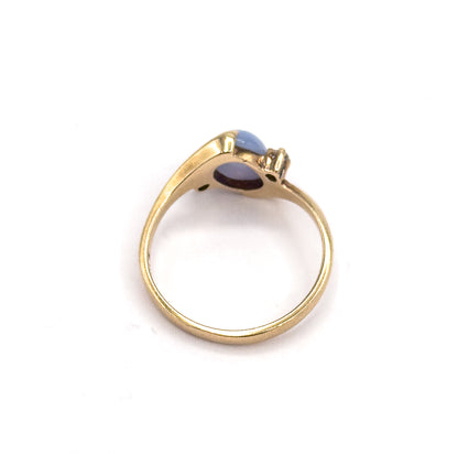 Rear view against white, looking through the open circle of the shank to the underside of the setting, where the back of the periwinkle cabochon and one small colourless spinel show.