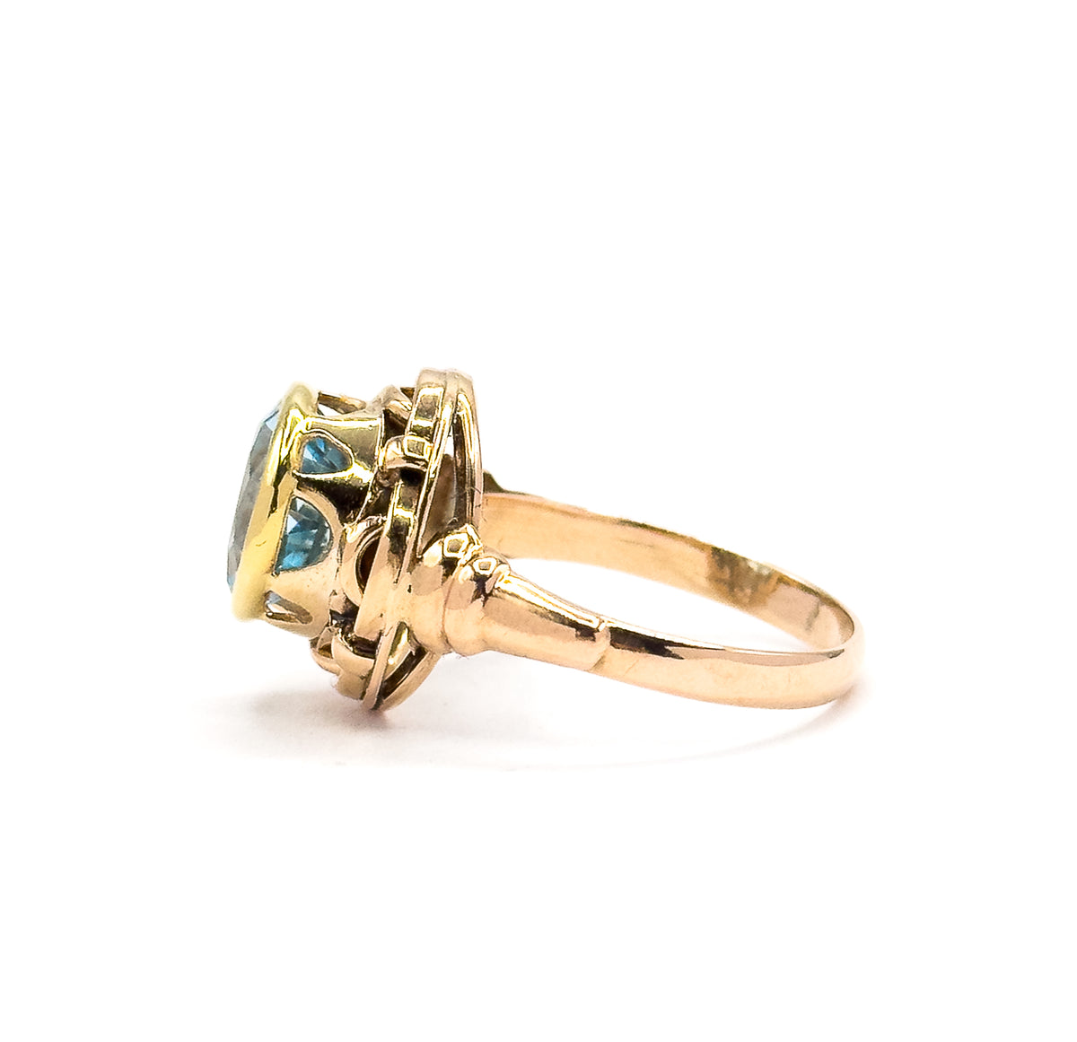 A full side profile, the slim rose gold shank sweeping up through flared shoulders to the raised knotwork gallery, with the blue topaz and its yellow gold bezel seen edge-on.