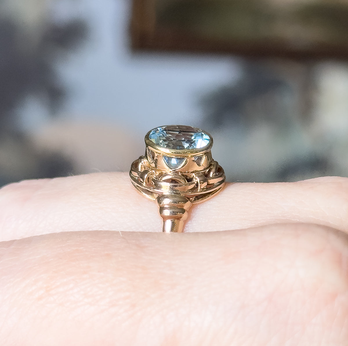 Retro Swiss blue topaz Celtic knot ring in 14K two-tone gold, shown on a finger in close-up, the round pale blue stone in a yellow gold bezel above interlaced rose gold knotwork and a slim shank.
