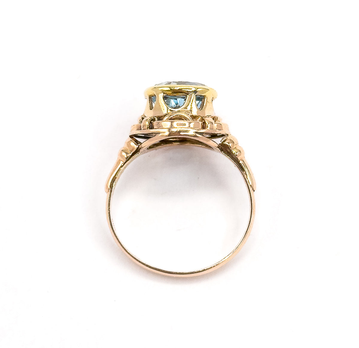 Stood upright and seen head-on through the open circle of the slim rose gold shank, the underside of the yellow gold bezel showing the blue stone through the pierced knotwork gallery.