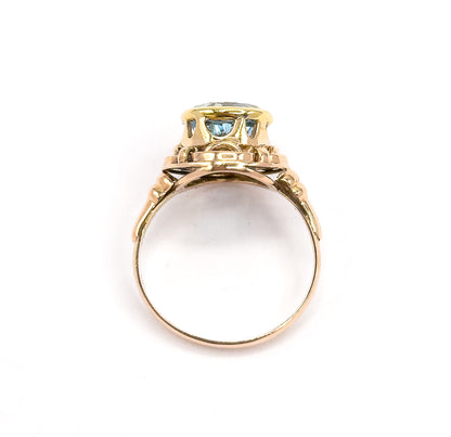 Stood upright and seen head-on through the open circle of the slim rose gold shank, the underside of the yellow gold bezel showing the blue stone through the pierced knotwork gallery.