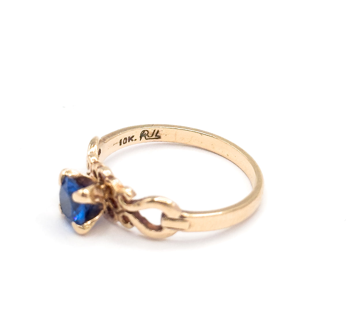 The ring tipped so the inside of the yellow gold shank faces up, its stamped markings across the top of the frame while the scrolled openwork shoulder and prong-set cobalt spinel angle down at lower left.