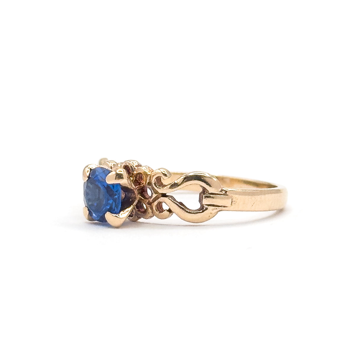 Straight profile view from the side, the cobalt spinel upright in its four prongs at left and the shoulder's open scrollwork forming a heart-shaped gap before the yellow gold shank tapers away.