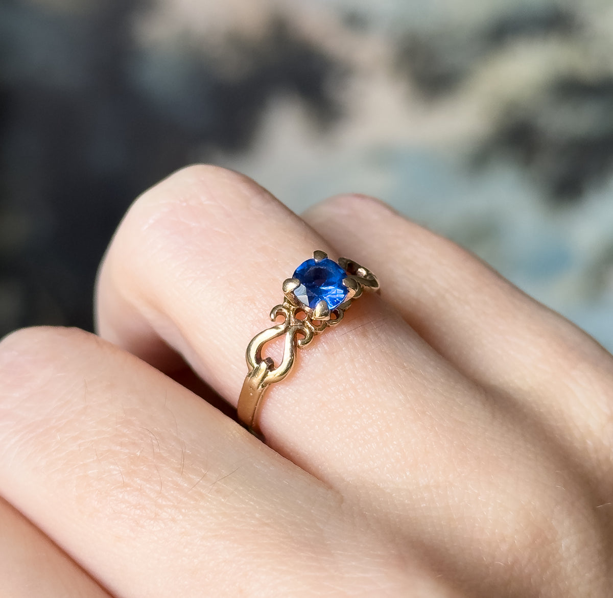 Angled side view on the finger, showing the low profile of the four-prong setting and the scrolled openwork gallery flowing into the tapering yellow gold shank.