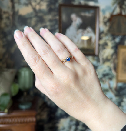 The whole hand is shown raised against a patterned backdrop, the ring small on the ring finger, giving a sense of its modest scale.