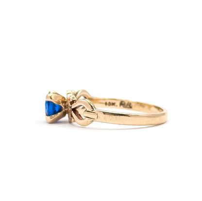 Close side view with the shank turned to the camera, showing small stamped markings struck inside the plain yellow gold band behind the scrolled shoulder and the prong-set cobalt spinel.