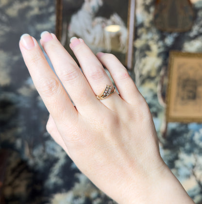 The hand is shown from the back against a blurred patterned backdrop, the ring low on the finger so its slim shank and small size read clearly.