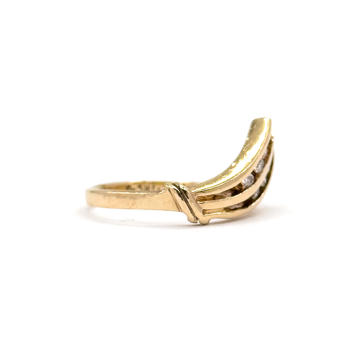 The ring lies almost flat in side view with the V-shaped face rising at the right, the plain yellow gold shank stretching left across the frame and the diamonds glinting along the upper bars.