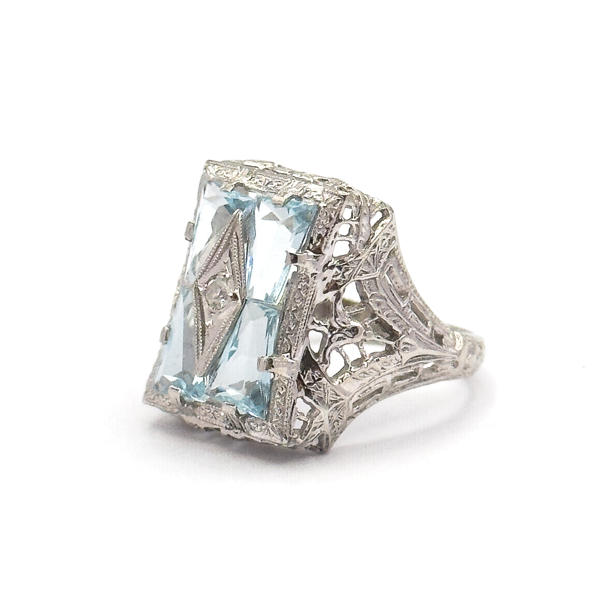 Three-quarter view with the face angled to the left, so the four icy blue aquamarines and their centre diamond are seen together with the openwork side panel and the shank tapering away to the right.