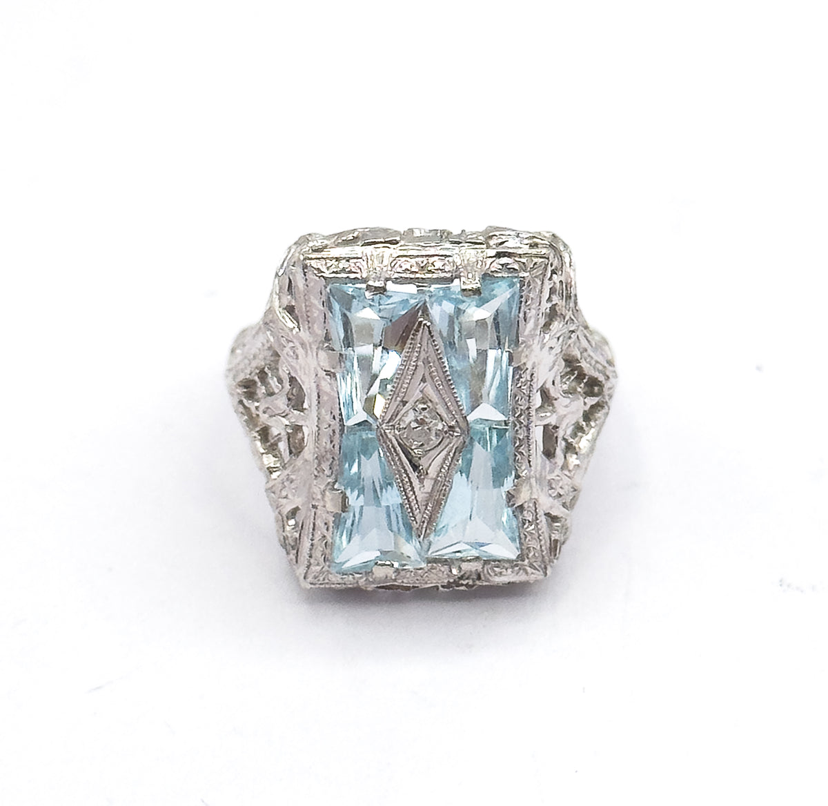 Straight down onto the rectangular face, the four icy blue aquamarines paired around a slim pointed centre panel holding the small diamond, with filigree shoulders flaring either side.