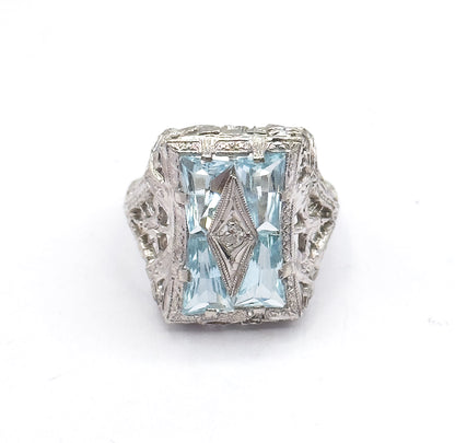 Straight down onto the rectangular face, the four icy blue aquamarines paired around a slim pointed centre panel holding the small diamond, with filigree shoulders flaring either side.