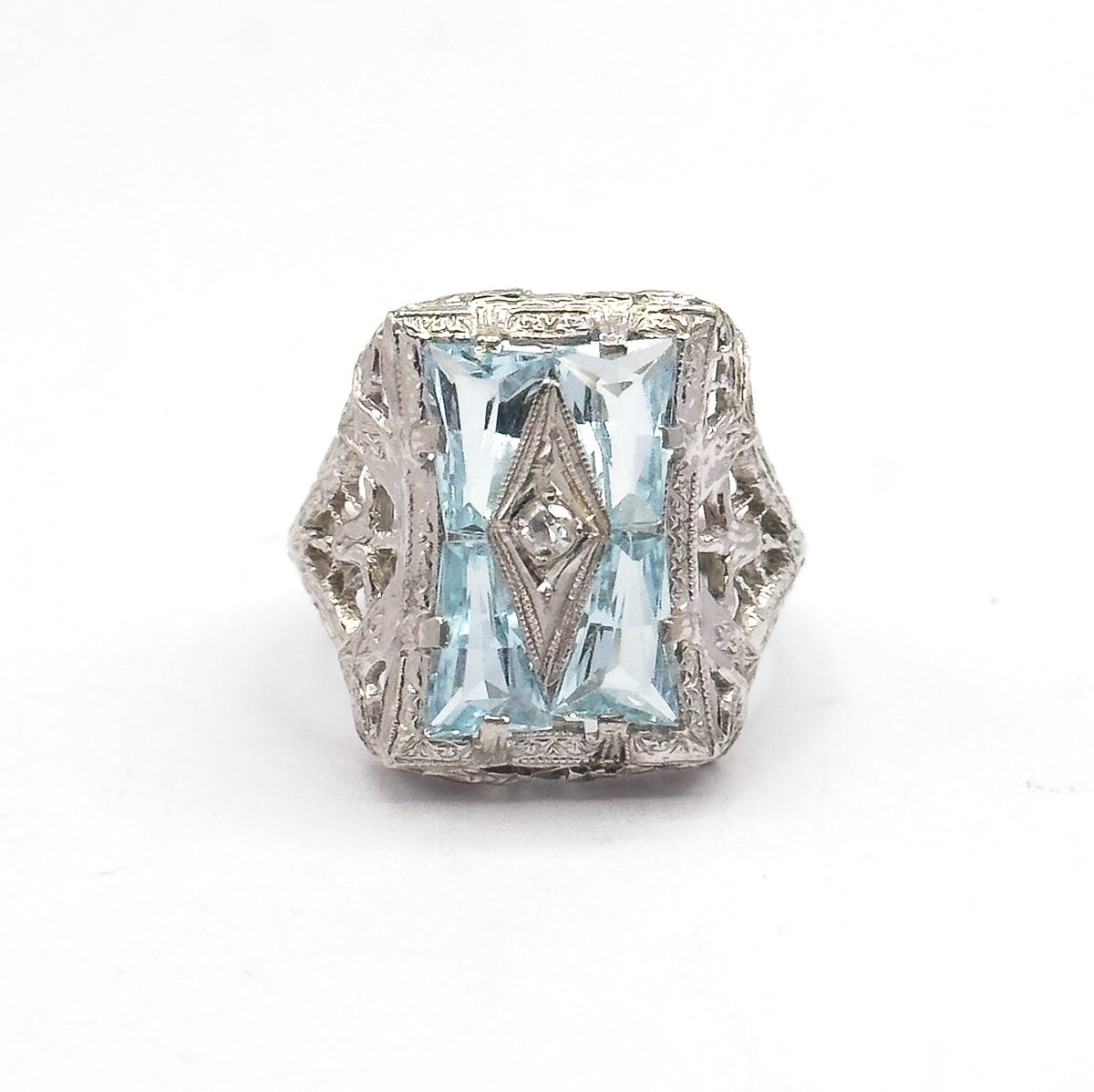 Front-on at eye level with the face upright, the engraved border framing the four icy blue aquamarines and their tiny centre diamond, and the pierced white gold shoulders flaring out on both sides.