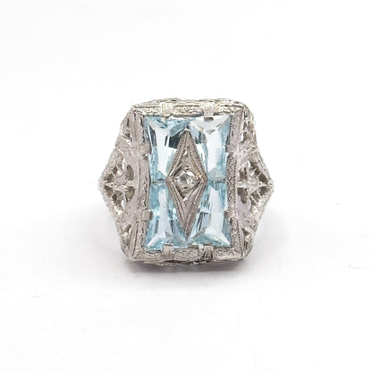 Front-on at eye level with the face upright, the engraved border framing the four icy blue aquamarines and their tiny centre diamond, and the pierced white gold shoulders flaring out on both sides.