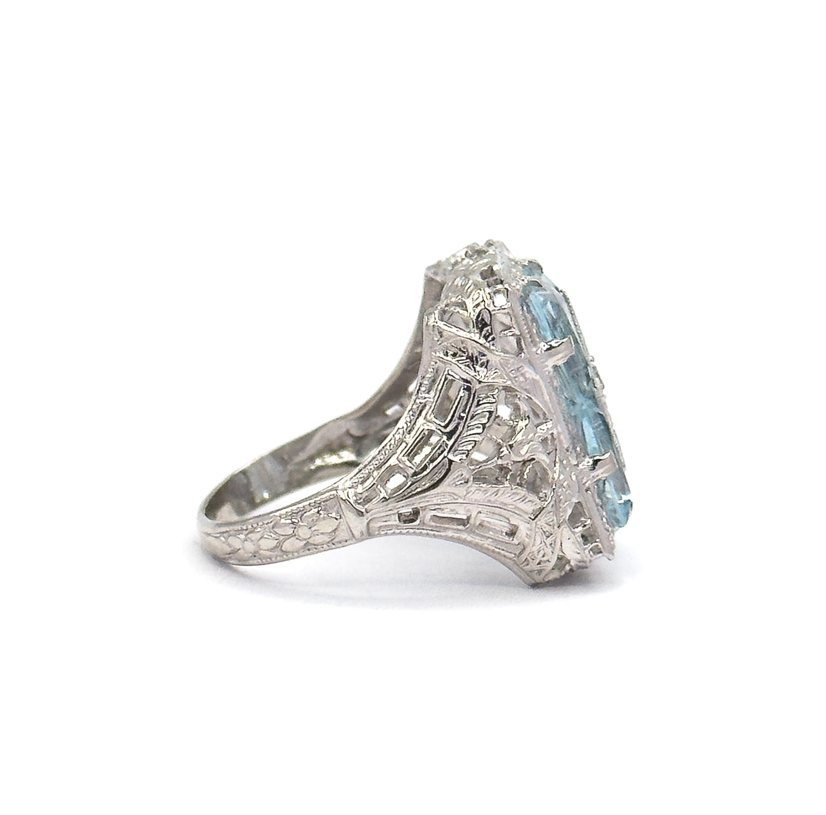 Full side profile against plain white, showing the flower-engraved shank rising through the filigree shoulder to the tall gallery, with the aquamarines seen edge-on at the top.