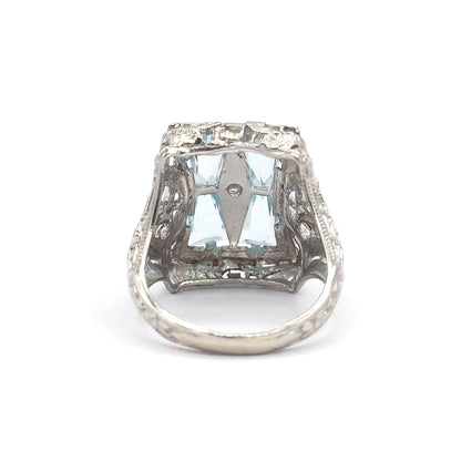 Closer view into the back of the head, where the aquamarines glow pale blue behind a pierced cross-bar holding the small centre stone, with the shank sweeping away below.
