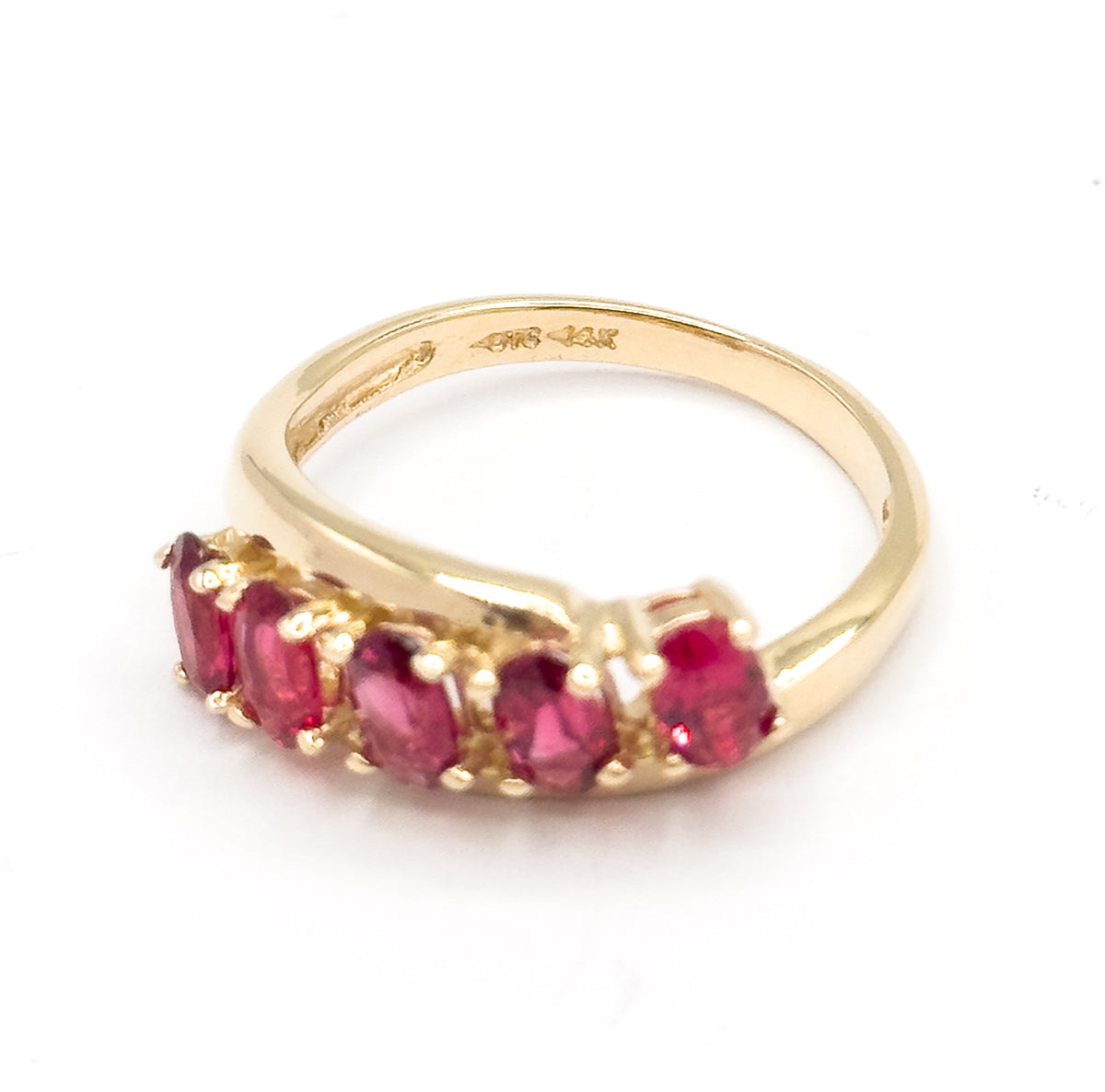 Tilted view against white looking into the open shank, where small stamped marks sit inside the yellow gold band above the row of five oval red spinels in their prongs.
