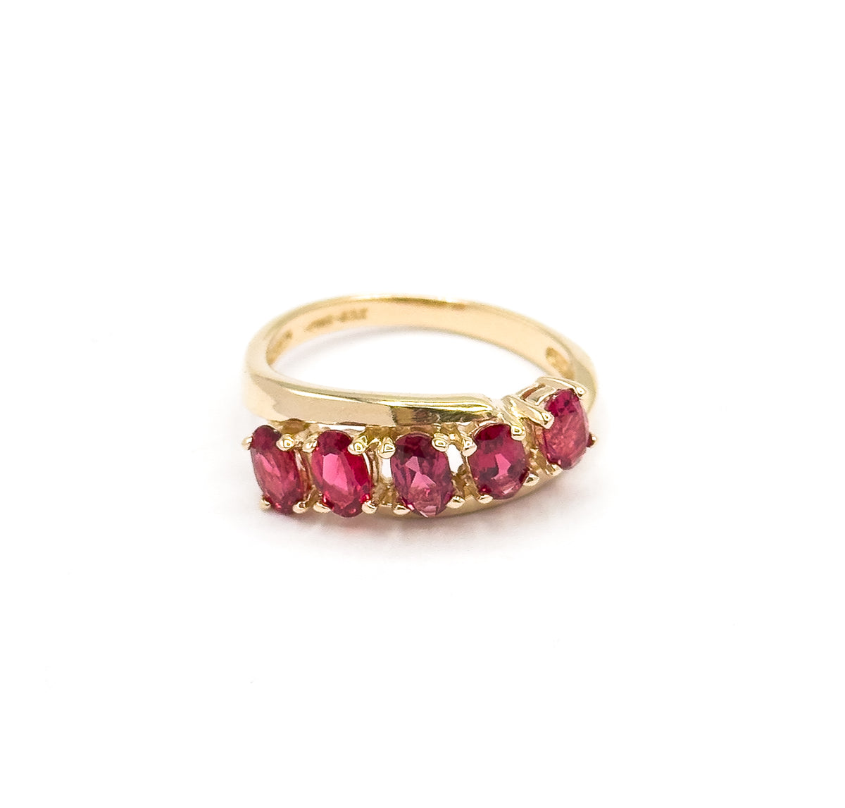 Low front-on view against white with the ring standing upright, the five oval red spinels curving in a gentle wave across the face while the slim yellow gold shank arches behind them.