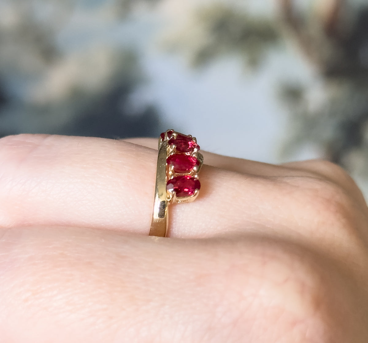 Red spinel five-stone ring in 14K yellow gold, shown on a finger from the side, its prong-set oval stones sweeping in a slight wave above the smooth tapering shank.