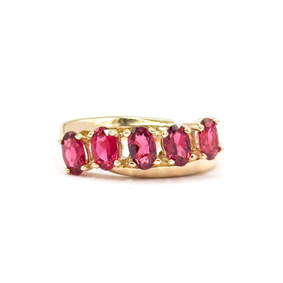 Off the hand against white, the ring stands upright so the five oval red spinels line up in a gentle wave, each held by small yellow gold prongs along the band.