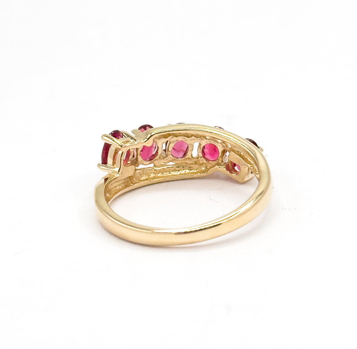 Rear view against white showing the open yellow gold gallery beneath the stone row, with the undersides of the oval red spinels visible through the pierced backing above the slim shank.
