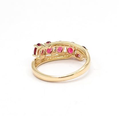 Rear view against white showing the open yellow gold gallery beneath the stone row, with the undersides of the oval red spinels visible through the pierced backing above the slim shank.