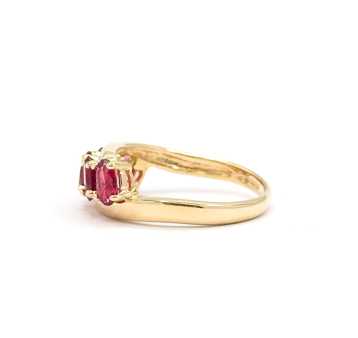 Side profile against white from behind the shank, the slim yellow gold band sweeping back from the stone row where two red spinels and their prongs sit at the left edge.