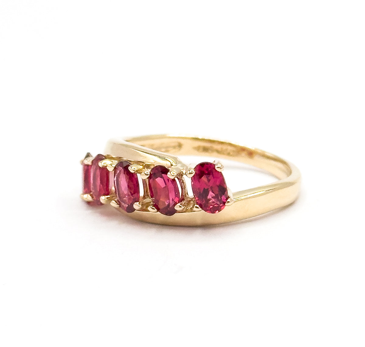 Angled three-quarter view against white, looking down the length of the shank so the five oval red spinels step away in a diagonal line, each prong catching the light.