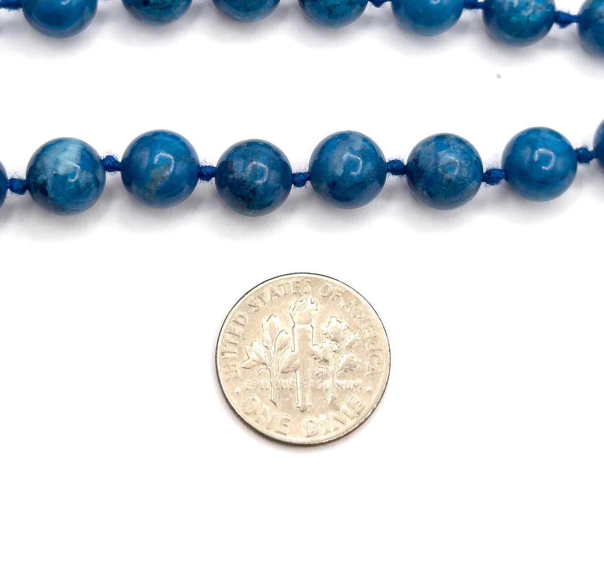 Two rows of the knotted strand laid flat on white with a dime placed below them, showing each round cobalt blue bead to be a little under a third of the coin's width.